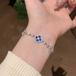 Detailed view of a silver-tone bracelet with blue clover charm and zircon inlay on wrist