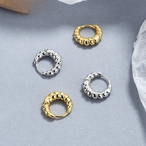 Detail of twisted hoop earrings in gold and silver finishes on a textured stone surface