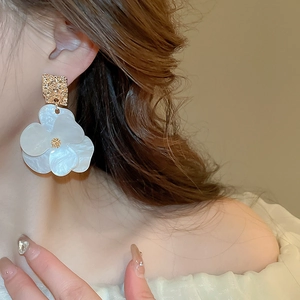 Close-up of a model wearing a white acrylic flower earring with golden textured metal top