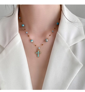 Close-up of stone beaded necklace with cross pendant on a model wearing a white blazer