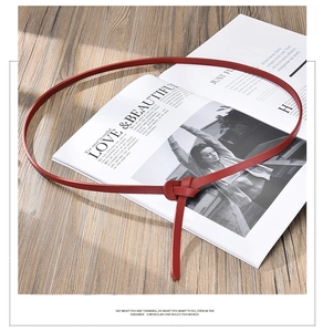 Detail of slim red knotted leather belt placed over a magazine on wood background