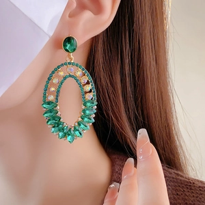 Detailed view of large vintage gold earrings with green crystals worn by a model