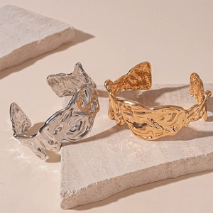 Irregular textured gold and silver cuff bracelets on a minimalist stone display