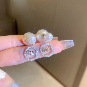 Macro shot of silver pearl earrings with zircon encrusted round pendant and miu logo