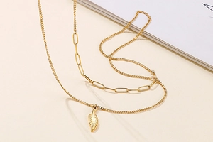 Detail view of gold double-layer necklace with paperclip chain and feather pendant