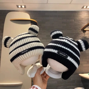 Detail of knitted baby hat featuring striped pattern, bear ears, and leather design label