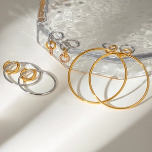 Boucles d'oreilles créoles en acier poli, finitions or et argent sur un plateau en verre