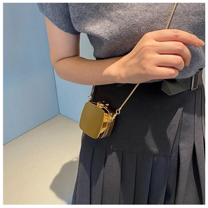 Close-up of a mini gold hard shell crossbody bag with metal chain on a model