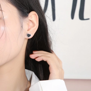 Close-up of minimalist black heart stud earrings on model with polished silver border