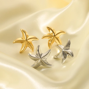 Gold and silver stainless steel starfish stud earrings on silk fabric background