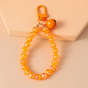 Close-up of orange aurora beaded keychain with a metal bell on a beige pedestal