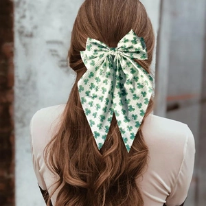 Detail of a large white bow hair clip with green shamrock and polka dot prints on wavy hair