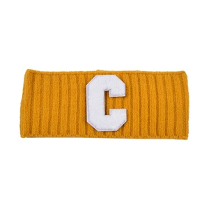 Détail du bandeau en maille côtelée jaune gingembre avec écusson lettre C blanc en chenille