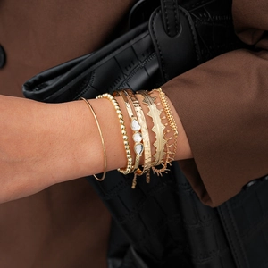 Detailed view of seven-piece gold bracelet set with rhinestones on female model