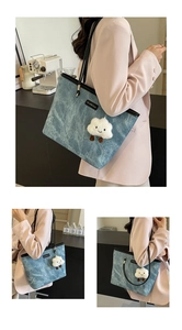 Detail of blue denim tote bag with black handles and cute white cloud plush pendant