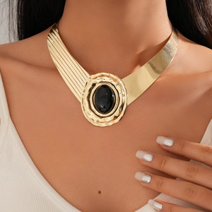 Close-up of a wide gold metal choker necklace with a central black oval stone on model