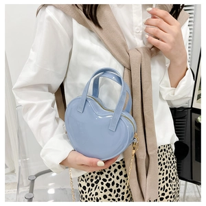 Detail of light blue heart-shaped jelly bag with gold chain strap on a model
