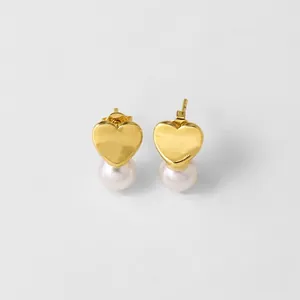 Macro detail of golden heart studs with polished finish and round white pearls