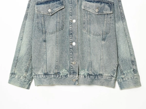 Detail of light blue washed denim jacket featuring heavy distressing and metal buttons