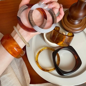 Close-up of retro iridescent resin and wood bracelets displayed on a ceramic dish