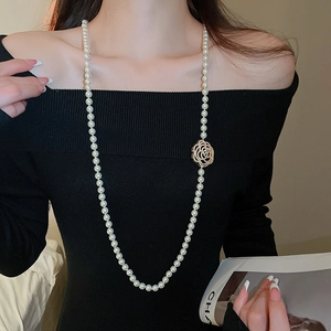 Détail d'un long collier de perles avec un charme de fleur de camélia doré sur un pull
