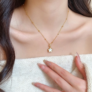 Detail shot of a star shaped gold pendant with white enamel inlay on a beaded gold chain