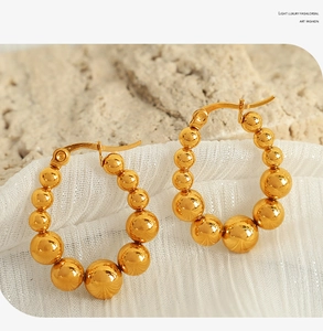 Close-up of golden beaded hoop earrings on a marble stone with elegant fabric texture