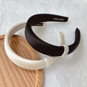 Padded satin headband with pearl detail and handmade silver logo on white paper background