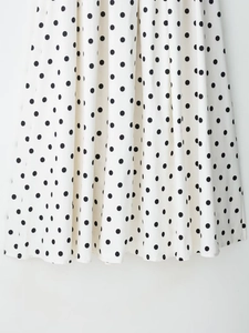 Détail du tissu blanc à pois noirs montrant la texture lisse et le drapé de la jupe