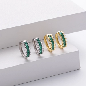 Detail view of gold and silver huggie earrings featuring claw-set emerald green zircons