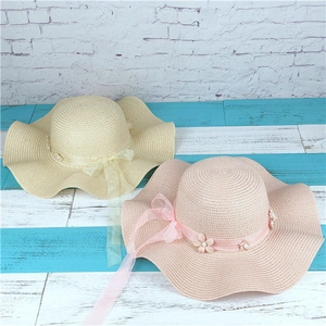 Detail view of wavy brim straw hats with silk bows and pearl flowers in beige and pink