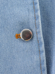 Close-up of light blue denim fabric with silver buttons and orange contrast stitching