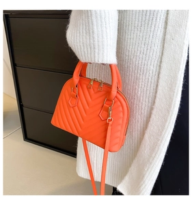 Detailed macro of bright orange quilted shell bag with gold hardware and plush outfit