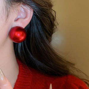 Close-up of a large glossy red spherical earring worn by a model in a red sweater