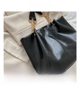 Vue détaillée du tissu brillant du sac noir avec chaîne dorée et texture souple