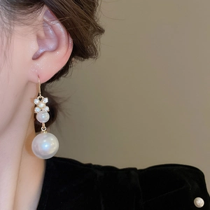 Dettaglio di orecchini a fiore dorati con perle e diamanti indossati da una modella
