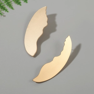 Detail view of gold wing-shaped earrings with matte textured finish and wavy edges