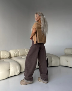 Dettaglio dei jeans a zampa marroni a vita bassa con un gilet in maglia strutturata