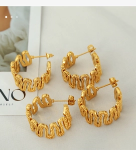 Detailed view of two pairs of gold C-shaped wavy textured hoop earrings on a magazine