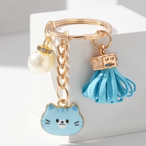 Detail of a gold cat keychain featuring a blue enamel charm, tassel, and white pearl