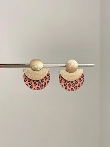 Close-up of geometric earrings with gold brushed metal and pink leopard print drops
