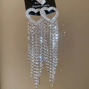 Macro shot of silver heart tassel earrings with sparkling rhinestones on black card