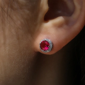 Macro close-up of a silver halo stud earring with a red gemstone and white zirconias