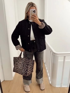 Close-up of black quilted jacket featuring trendy leopard print cuffs and button closure