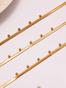 Detailansicht der goldenen Schlangenkette mit kleinen Perlen auf weißem Grund