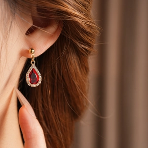 Close-up of elegant gold drop earring with red gemstone and sparkling zirconia on ear