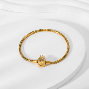 Detail of 18K gold snake chain bracelet with crystal-studded crown clasp on white background