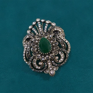 Vintage bronze brooch with teardrop green gemstone and crystals on dark texture