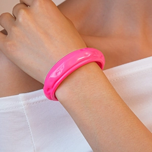 Dettaglio del bracciale in acrilico rosa neon con trama ondulata sul polso del modello