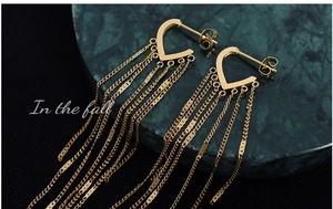 Macro view of long gold tassel earrings with heart-shaped studs on green marble